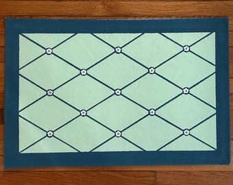 May include: A green and blue rug with a diamond pattern and white flowers. The rug has a dark blue border.