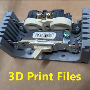 May include: A gray 3D-printed electrical outlet cover with an electrical outlet installed. The text "3D Print Files" is in yellow at the bottom of the image. The outlet has a beige face and metal components.