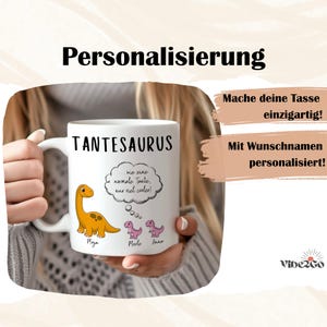 May include: White ceramic mug with the word "TANTESAURUS" in black. The mug features a cartoon dinosaur and the text "...wie eine normale Tante, nur viel cooler!" in a thought bubble. Additional text includes names and the word "Personalisierung".