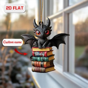 May include: A black dragon ornament with red eyes and wings sits atop a stack of books. The books are various colors, and the name "Henry" is printed on the top book. The ornament is hanging by a gold string. The text "2D FLAT" and "Custom name" are also visible.