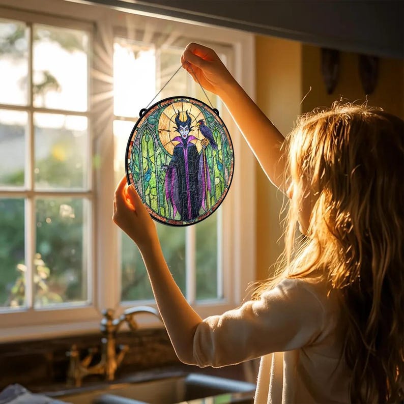 Puede incluir: Arte de ventana de vidriera redonda con un personaje morado y negro con un cuervo. La obra de arte tiene un borde negro y est&aacute; suspendida por una cuerda negra. El fondo incluye un dise&ntilde;o de vidriera con tonos verdes y amarillos.