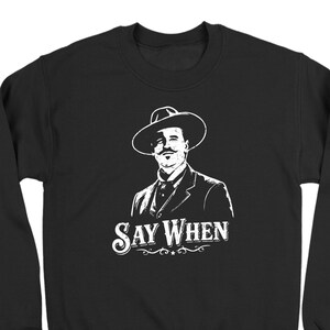May include: Black crewneck sweatshirt with a white graphic of a man in a hat and suit, with the text "Say When" in a decorative font. The design is a vintage-inspired illustration.