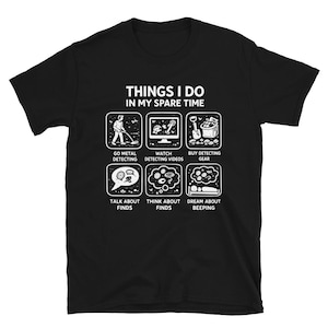 以下が含まれることがあります： THINGS I DO IN MY SPARE TIMEという白いグラフィックテキストがプリントされた黒い半袖Tシャツ。テキストの下には、金属探知活動を描いた6つの正方形のイラストがあり、GO METAL DETECTING、WATCH DETECTING VIDEOS、BUY DETECTING GEAR、TALK ABOUT FINDS、THINK ABOUT FINDS、DREAM ABOUT BEEPINGというラベルが付いています。