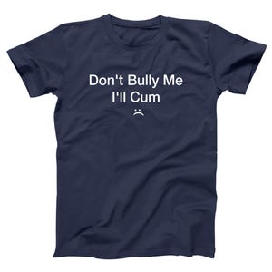 May include: Navy blue t-shirt with the text "Don't Bully Me I'll Cum" in white, along with a small, sad face emoji. The shirt is a casual wear item.