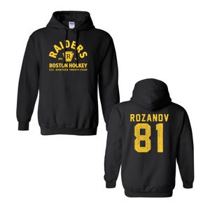 May include: A black hooded sweatshirt featuring yellow graphics. The front displays the text RAIDERS BOSTON HOCKEY EST. NINETEEN TWENTY-FOUR with a shield logo. The back features the name ROZANOV and the number 81 in a distressed yellow font.