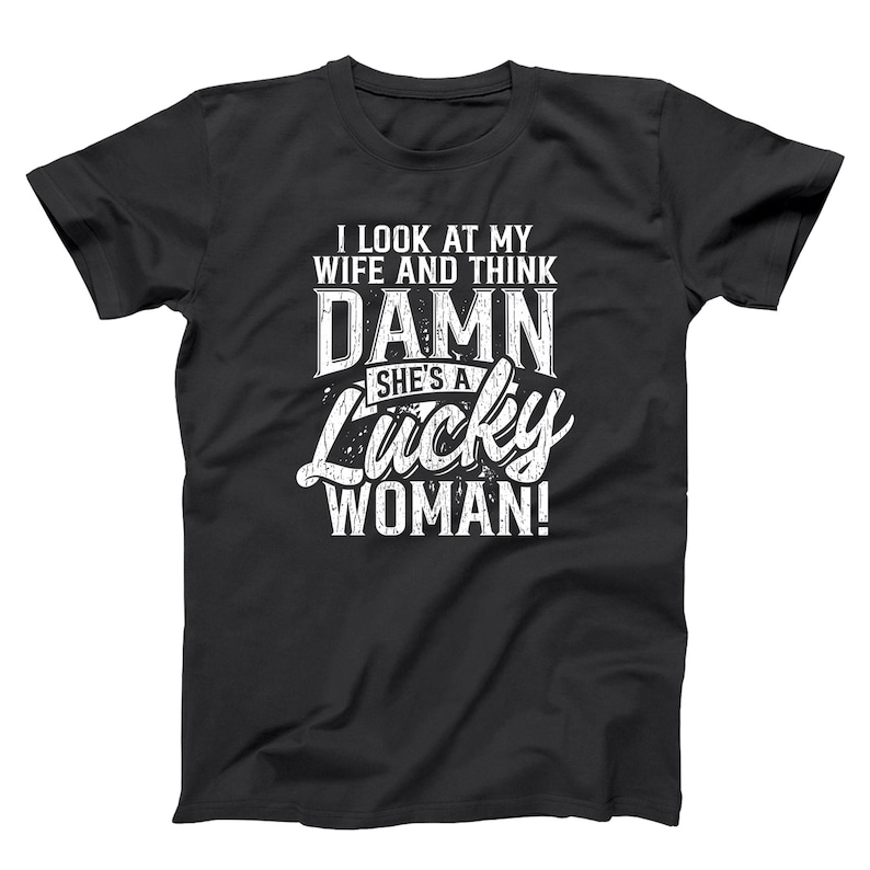 May include: Black t-shirt with white text that reads "I LOOK AT MY WIFE AND THINK DAMN SHE'S A Lucky WOMAN!" The text is in a bold, stylized font. The shirt is a crew neck style.