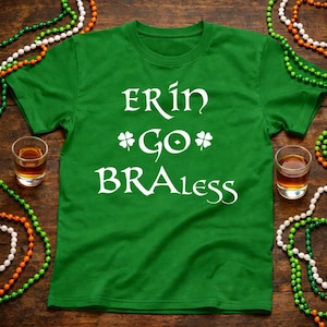 May include: Green t-shirt with the text "ERIN GO BRALess" in white, with shamrock symbols. Two shot glasses with amber liquid and beaded necklaces in green, white, and orange are on a wooden surface.