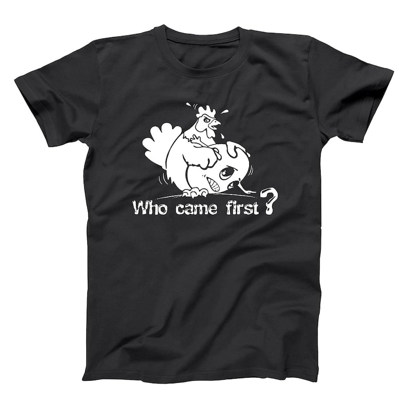 May include: Black t-shirt with a white graphic of a chicken looking at a cracked egg. The text "Who came first?" is below the graphic. The design is a humorous take on the classic chicken or the egg riddle.