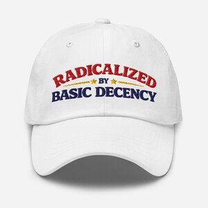 May include: White baseball cap featuring the embroidered text "RADICALIZED by BASIC DECENCY" in red and blue. The text is arched, with gold stars and a gold line separating the words, on the front of the cap.