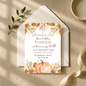 Puede incluir: Una tarjeta de invitación blanca con el texto "OH WHAT FUN Our little PUMPKIN is turning ONE" y una ilustración de calabaza. La tarjeta está rodeada de elementos florales con temática otoñal y está dentro de un sobre blanco.