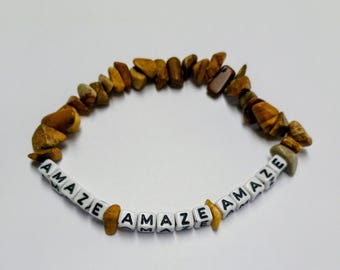 May include: A bracelet made of irregular, polished brown and tan stone chips interspersed with white square beads featuring the black printed text AMAZE. The beads are arranged in a repeating pattern with the word AMAZE appearing multiple times.