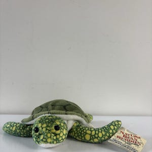 May include: A plush green sea turtle toy with a textured shell and flippers. The turtle has black eyes and a white underbelly. A tag is attached to the turtle.