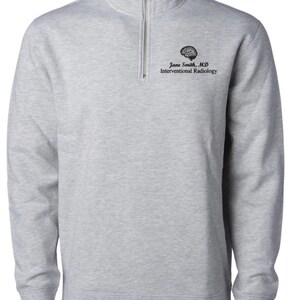May include: A light gray quarter-zip sweatshirt with a black embroidered brain graphic and text that reads "Jane Smith, MD Interventional Radiology". The sweatshirt has a ribbed collar, cuffs, and hem.