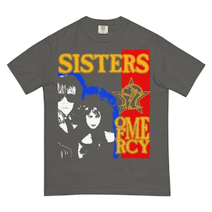 May include: Dark gray t-shirt featuring a graphic design with the text "SISTERS OF MERCY" in yellow and red. The design includes a star and two black and white portraits. The shirt is a crew neck and has a relaxed fit.