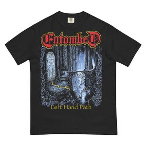 May include: Black t-shirt featuring the band name "Entombed" in red and yellow lettering above a detailed forest scene. The graphic includes a path and the text "Left Hand Path" in yellow.