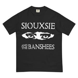 May include: Black t-shirt featuring the band name "Siouxsie and the Banshees" in white block letters above a stylized white graphic of two eyes. The shirt is a classic crew neck style.