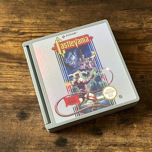 Könnte beinhalten: Castlevania Videospielkassette für das Nintendo Entertainment System. Die Spielbox zeigt einen Krieger mit einer Peitsche, ein Schloss und eine dämonische Figur. Die Logos von Konami und Nintendo sind sichtbar.
