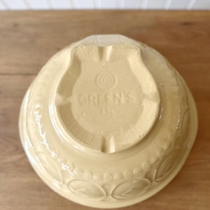 K&ouml;nnte beinhalten: Eine hellgelbe R&uuml;hrsch&uuml;ssel aus Keramik mit gepr&auml;gten Bl&auml;ttermustern am Rand. Der Boden der Sch&uuml;ssel tr&auml;gt den Text "GREEN'S" in einem schildf&ouml;rmigen Design. Ein Vintage-K&uuml;chenartikel.