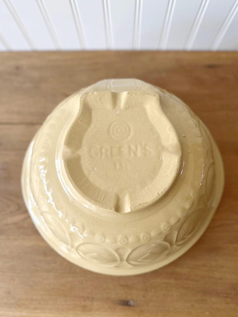 K&ouml;nnte beinhalten: Eine hellgelbe R&uuml;hrsch&uuml;ssel aus Keramik mit gepr&auml;gten Bl&auml;ttermustern am Rand. Der Boden der Sch&uuml;ssel tr&auml;gt den Text "GREEN'S" in einem schildf&ouml;rmigen Design. Ein Vintage-K&uuml;chenartikel.