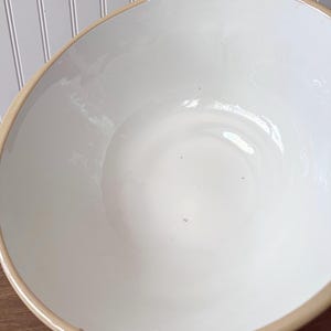K&ouml;nnte beinhalten: Eine gro&szlig;e, cremefarbene Keramiksch&uuml;ssel mit hellem braunen Rand. Die Sch&uuml;ssel hat eine glatte, gl&auml;nzende Oberfl&auml;che und eine breite, flache Form. Das Innere ist strahlend wei&szlig; und kontrastiert mit der Farbe des Randes.