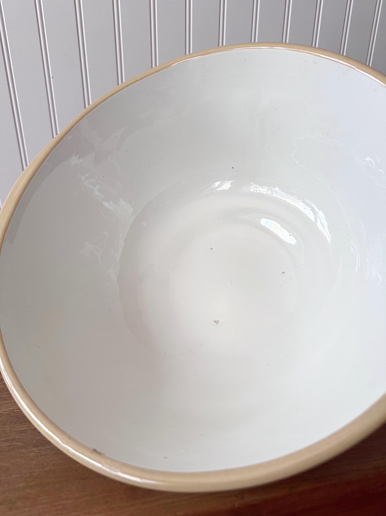 K&ouml;nnte beinhalten: Eine gro&szlig;e, cremefarbene Keramiksch&uuml;ssel mit hellem braunen Rand. Die Sch&uuml;ssel hat eine glatte, gl&auml;nzende Oberfl&auml;che und eine breite, flache Form. Das Innere ist strahlend wei&szlig; und kontrastiert mit der Farbe des Randes.
