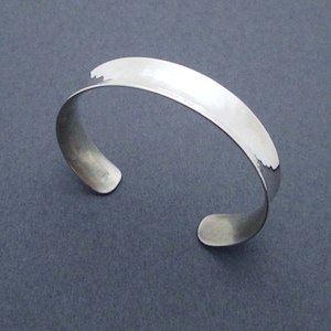May include: A silver cuff bracelet with a smooth, polished finish. The bracelet is open and has a slightly curved shape.