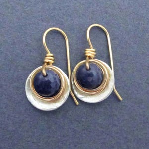 May include: A pair of gold and silver earrings with a dark blue gemstone in the center of each earring.