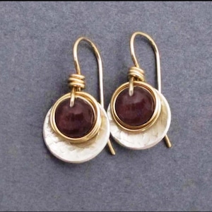 May include: A pair of silver and gold earrings with a round, dark purple gemstone in the center of each earring.