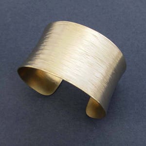 May include: A wide gold metal cuff bracelet with a brushed finish.