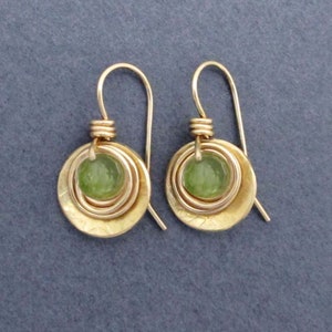May include: Gold earrings with a green stone set in a circle of gold wire. The earrings have a hammered finish.