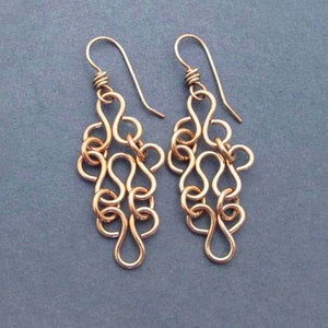 May include: A pair of gold-toned dangle earrings with a delicate, intricate chain design. The earrings are made of multiple interconnected loops, creating a flowing and elegant look.