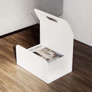 May include: A white magazine holder with a handle, holding a stack of magazines. The magazines have a cover with the text "LF LOOS". The holder is on a wooden surface.