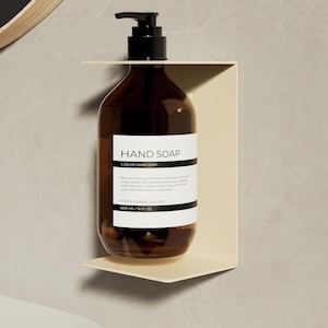 Könnte beinhalten: Eine braune Glasflasche für Handseife mit schwarzem Pumpspender, gehalten von einer cremefarbenen Wandhalterung aus Metall. Das weiße Etikett trägt den Text HAND SOAP, LIQUID HAND SOAP, 500 ML | 16 FL OZ sowie Anweisungen zur Anwendung.