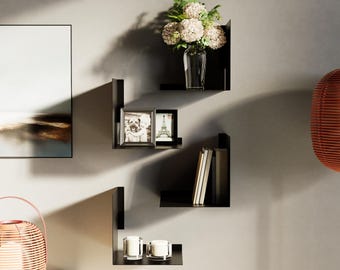 May include: Black floating shelves mounted on a gray wall, displaying a vase of flowers, framed photos, books, and candles. The shelves have a modern, minimalist design, creating a stylish storage and display solution for home decor.