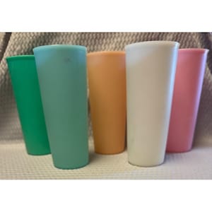 Puede incluir: Un conjunto de cinco vasos cilíndricos altos en una variedad de colores sólidos que incluyen verde brillante, verde azulado claro, naranja suave, blanco opaco y rosa pastel. Cada vaso presenta un acabado liso y un diseño cónico simple.