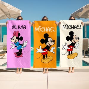 May include: Three beach towels featuring Mickey and Minnie Mouse. Each towel has a different background color: pink, orange, and cream. The pink towel has Minnie Mouse and the name "Olivia". The orange towel has Mickey Mouse and the name "Michael". The cream towel has Mickey Mouse and the name "Michael".