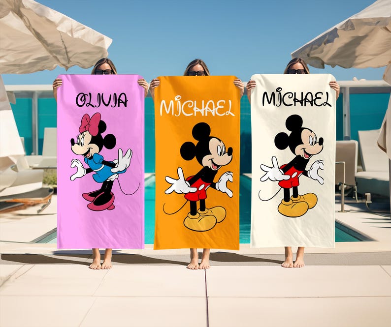 May include: Three beach towels featuring Mickey and Minnie Mouse. Each towel has a different background color: pink, orange, and cream. The pink towel has Minnie Mouse and the name "Olivia". The orange towel has Mickey Mouse and the name "Michael". The cream towel has Mickey Mouse and the name "Michael".