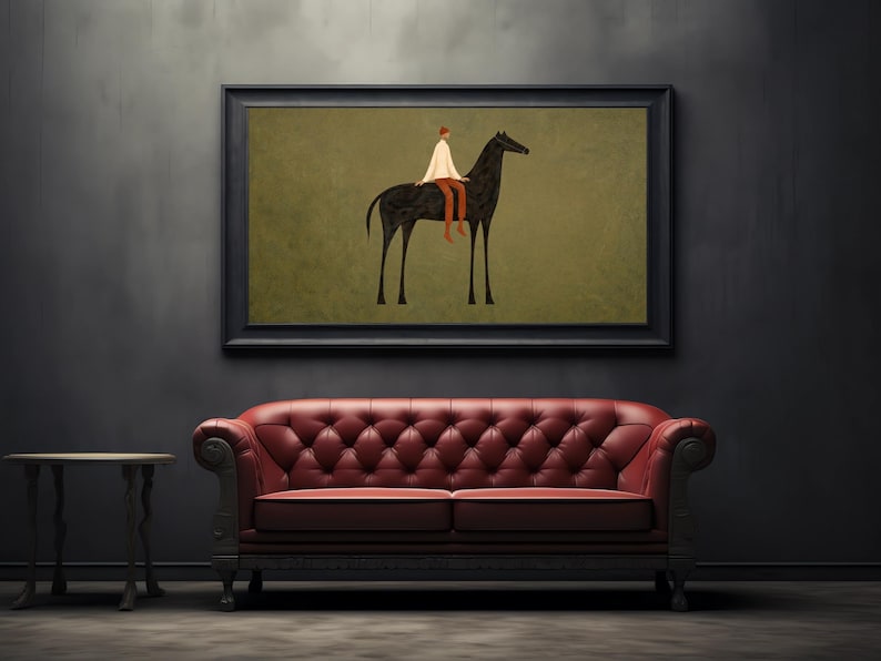 May include: An art print featuring a minimalist illustration of a person riding a black horse. The artwork is framed in black and hangs above a red tufted leather sofa. A small side table is to the left.