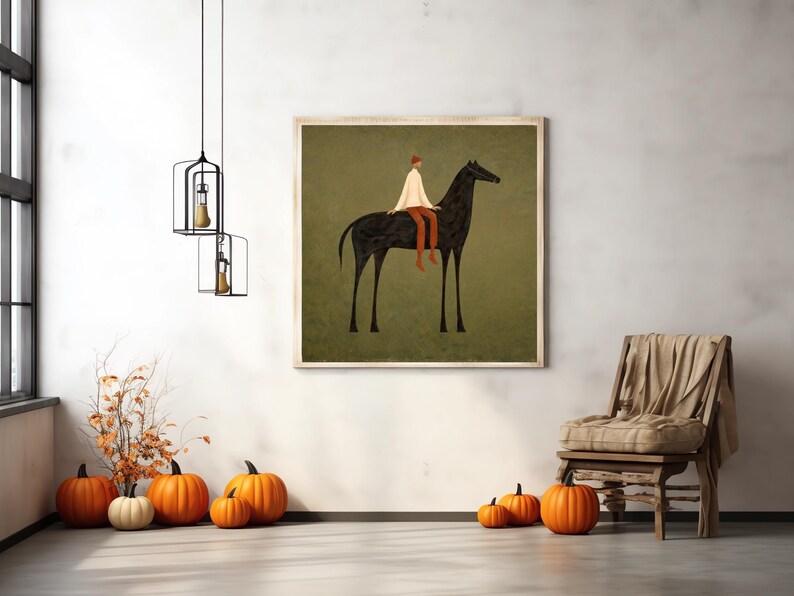 May include: A framed art print depicts a person riding a black horse against a muted green background. The rider wears a white top and orange pants. The room features pumpkins, a wooden chair, and hanging light fixtures.