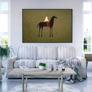 May include: A framed art print depicts a minimalist illustration of a person riding a black horse. The rider wears a white garment and brown pants against a muted olive green background. The artwork is displayed above a sofa in a living room.