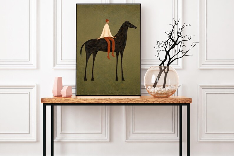 May include: An art print featuring a black horse with a rider in a white shirt, red pants, and a red hat. The artwork is set against a muted green background and framed in black. The print is displayed on a wooden table with a black metal frame, alongside decorative vases.