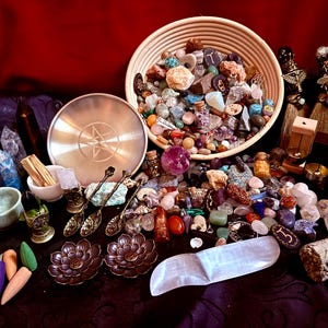 May include: A collection of crystals, stones, and spiritual items arranged on a dark surface. A woven basket overflows with colorful tumbled stones. Other items include a metal plate with a star design, incense cones, and decorative spoons.