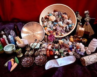 May include: A collection of crystals, stones, and spiritual items arranged on a dark surface. A woven basket overflows with colorful tumbled stones. Other items include a metal plate with a star design, incense cones, and decorative spoons.