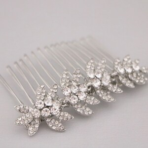 May include: Silver hair comb with a row of five crystal flower designs. Each flower has a center stone and smaller stones around it.