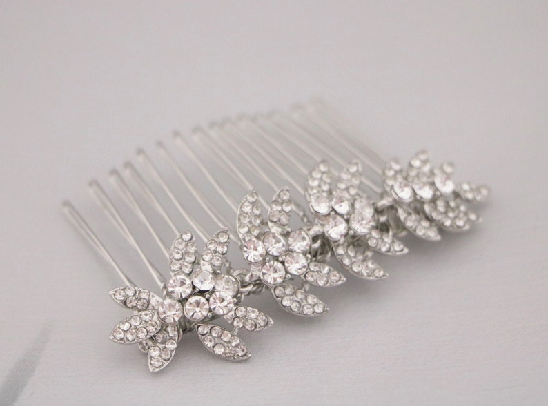 May include: Silver hair comb with a row of five crystal flower designs. Each flower has a center stone and smaller stones around it.