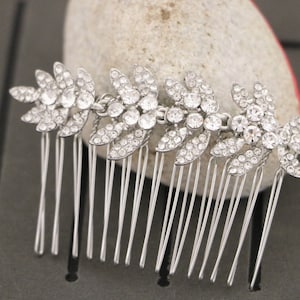 May include: Silver hair comb with a row of five crystal flower designs. Each flower is made of small, clear rhinestones.