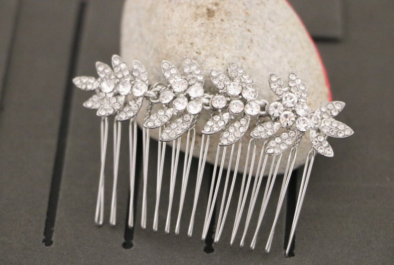 May include: Silver hair comb with a row of five crystal flower designs. Each flower is made of small, clear rhinestones.