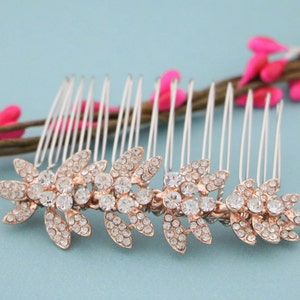 May include: A silver hair comb with a row of clear rhinestones in a floral design. The comb is decorated with rose gold accents.