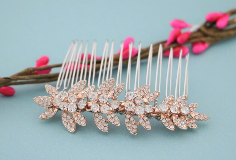 May include: A silver hair comb with a row of clear rhinestones in a floral design. The comb is decorated with rose gold accents.