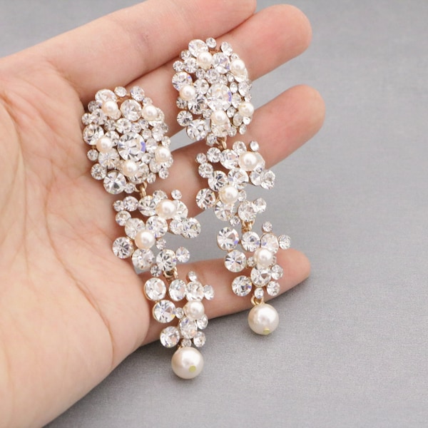 May include: A pair of gold tone dangle earrings with multiple layers of clear crystals and white pearls. The earrings are approximately 3 inches long.